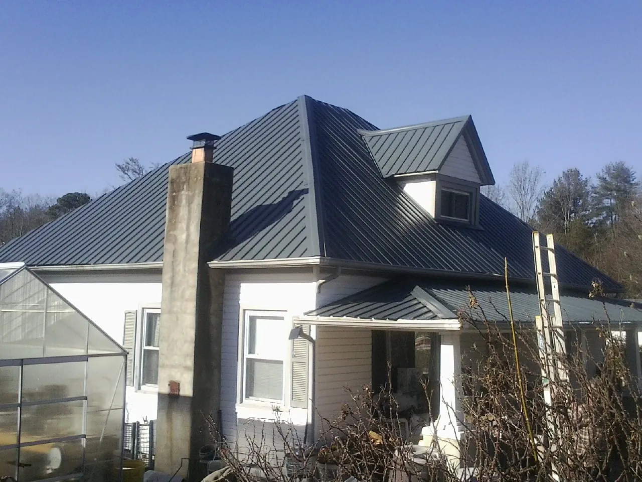 Dark blue standing seam metal roof on a white farmhouse with dormer — Slate & Tile Roof Repair by Roofing Brothers in Grapeville