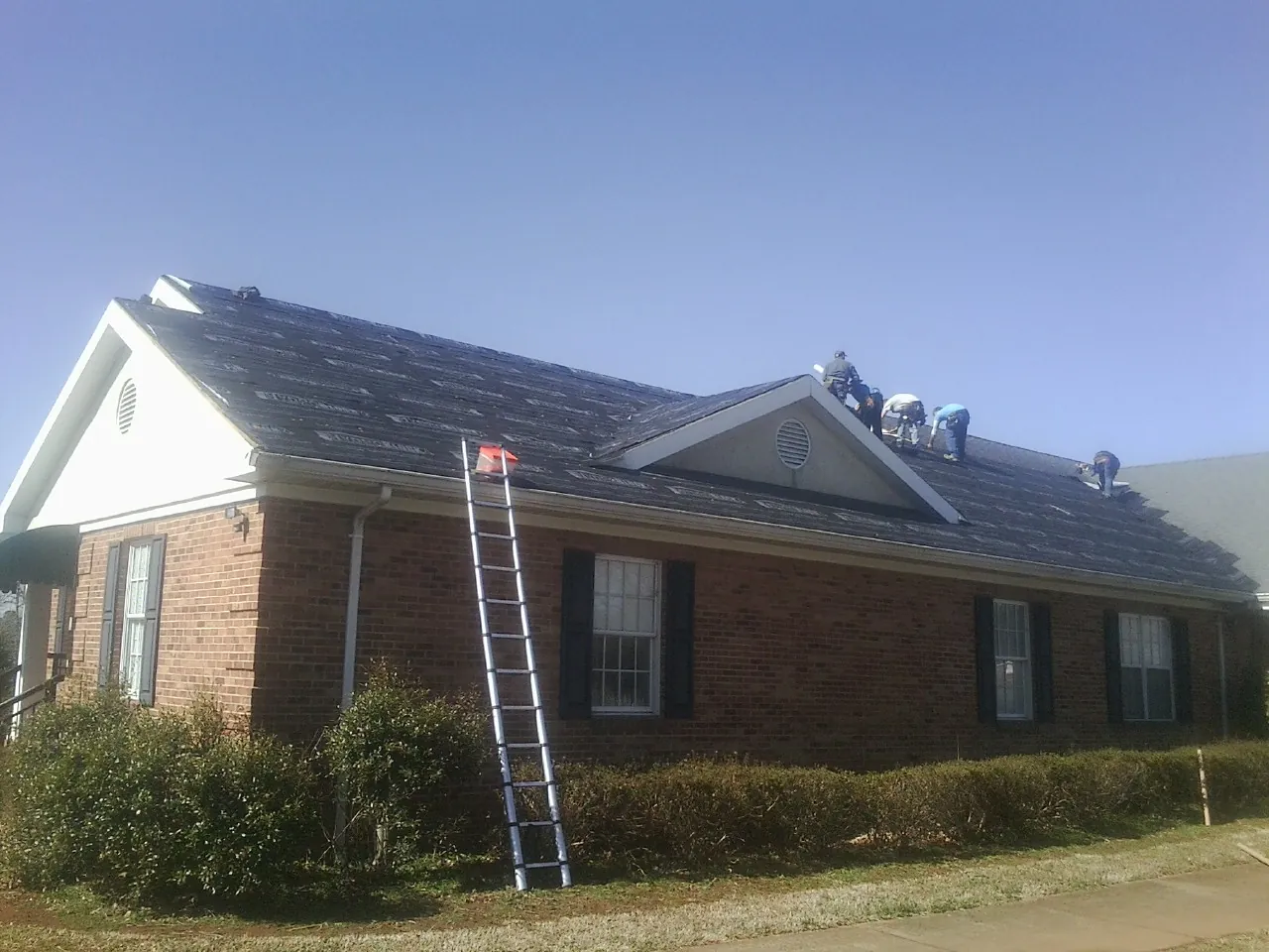 Crew tearing shingles off a brick ranch roof with a ladder set — Metal Roof Repair work by our crew in Grapeville