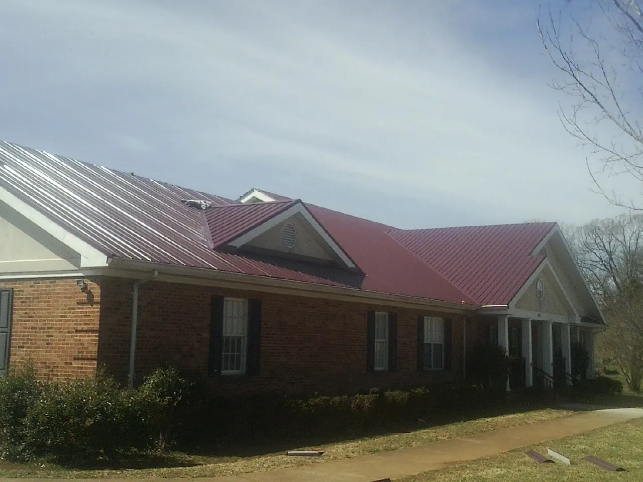 Red metal roof with gabled entries on a long brick building, from a Hail Damage Roof Repair job in Grapeville