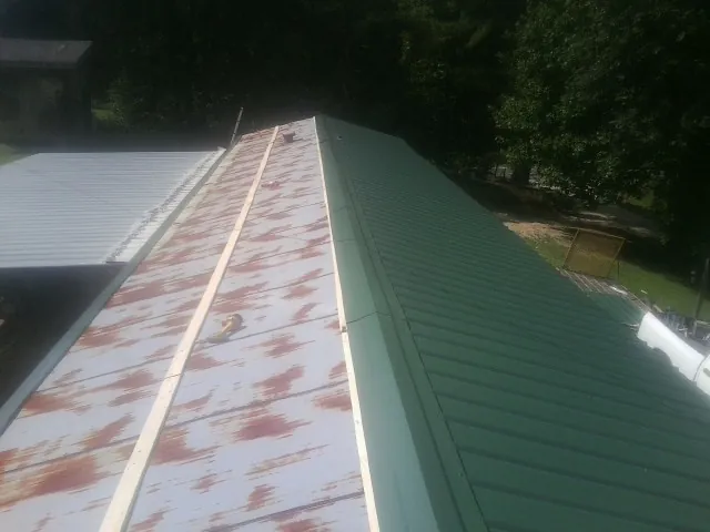 Old rusted panels beside newly installed green metal roofing — Wind Damage Roof Repair by Roofing Brothers in Grapeville