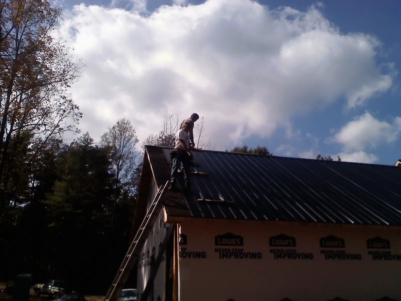 Roofer fastening dark metal panels high against a cloudy sky, from a Roof Inspection job in Grapeville