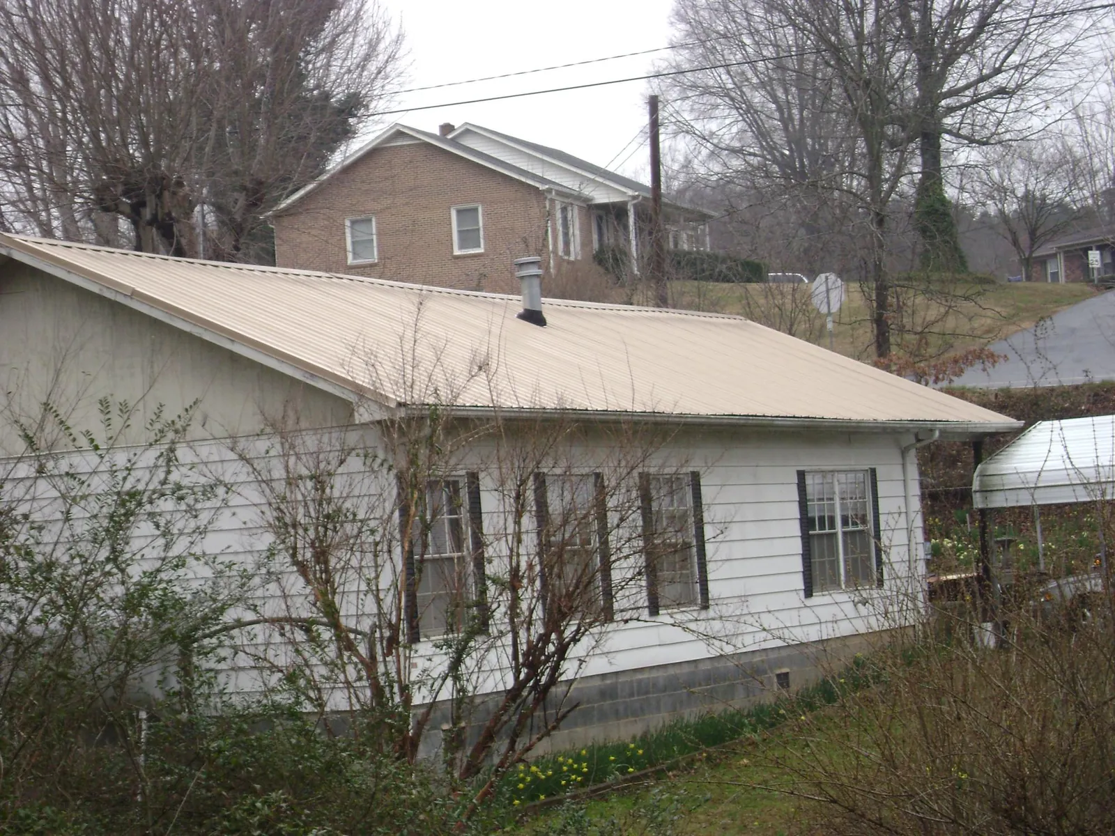 Tan metal roof on a white sided house set into a hillside — Commercial Roofing by Roofing Brothers in Grapeville