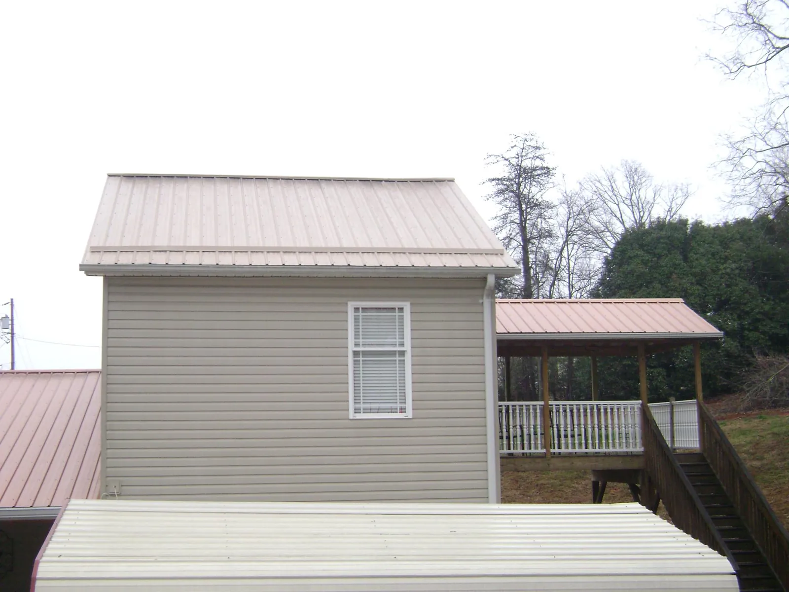 Tan metal roofs on a two story addition and attached porch, from a Roof Replacement job in Grapeville